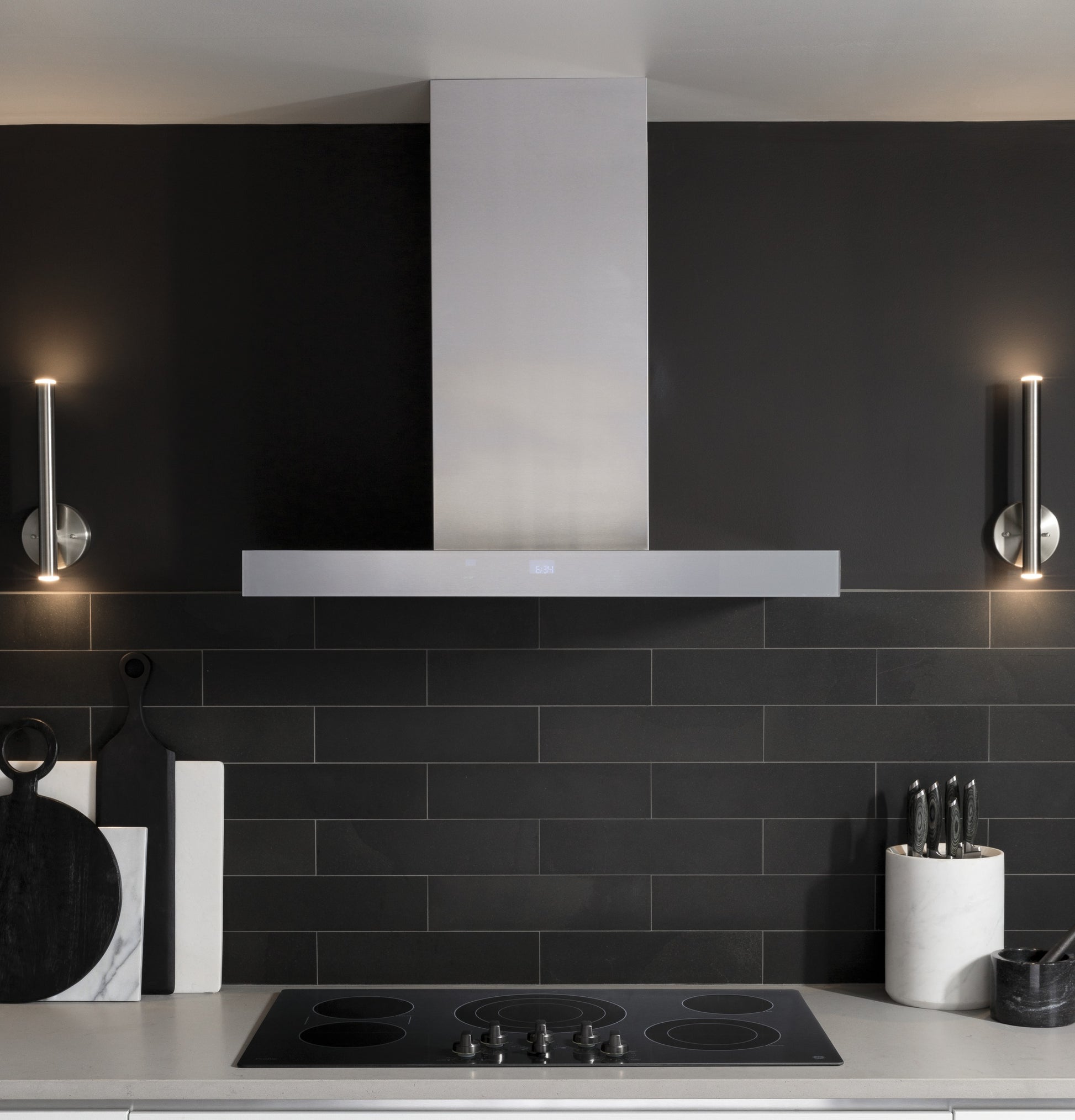 Sleek stainless steel wall mount hood with perimeter venting above electric cooktop in modern kitchen setting