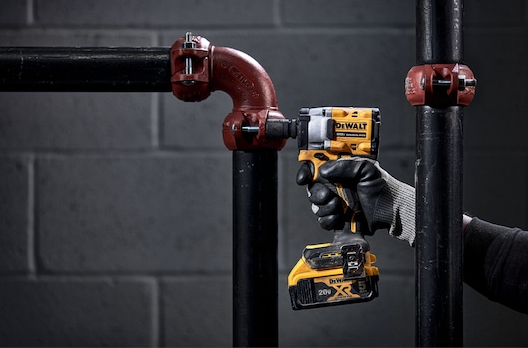 Person using yellow and black cordless impact wrench on black metal piping for tools and home improvement tasks