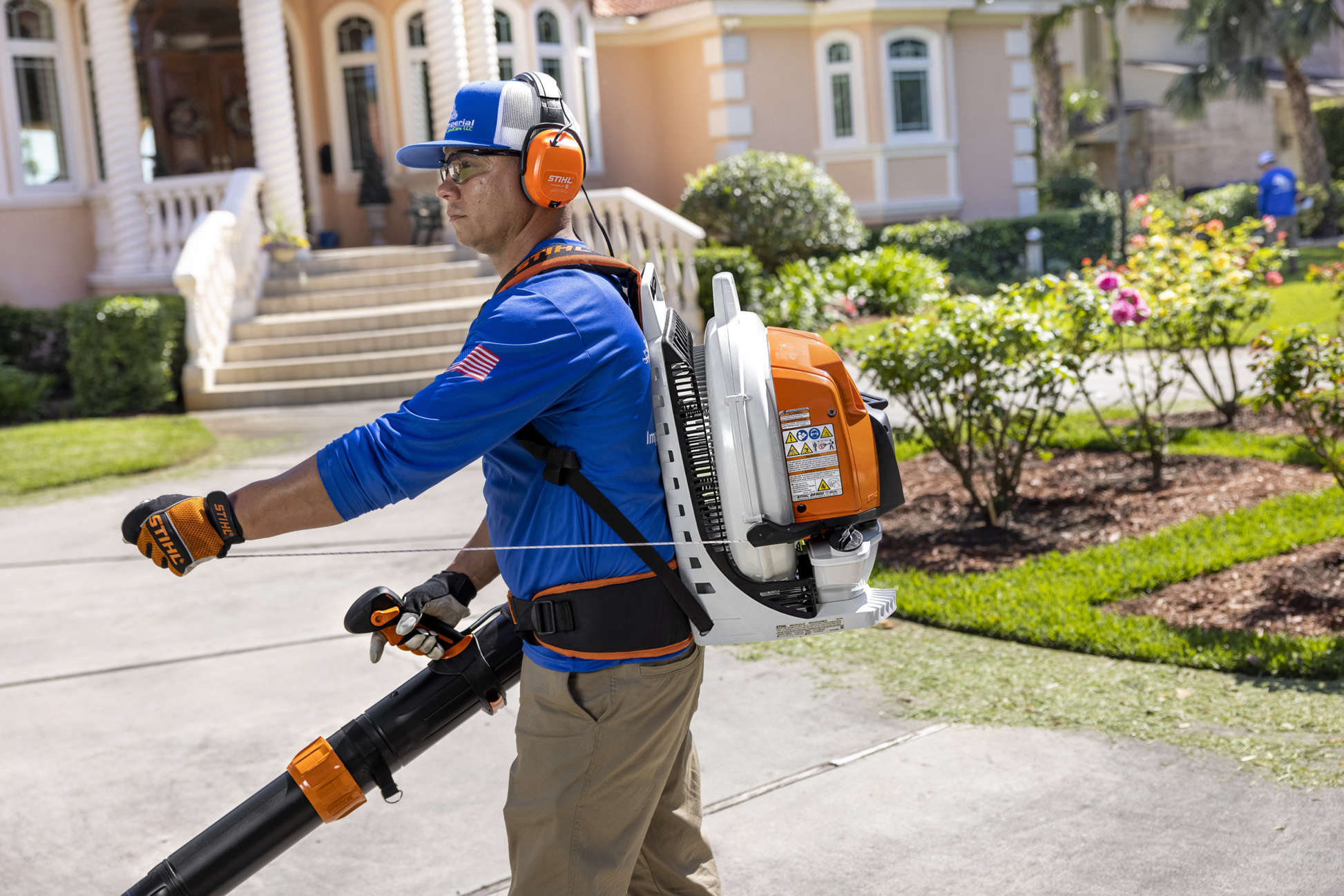 Professional wearing safety gear operating an orange and white backpack blower for outdoor home improvement tasks