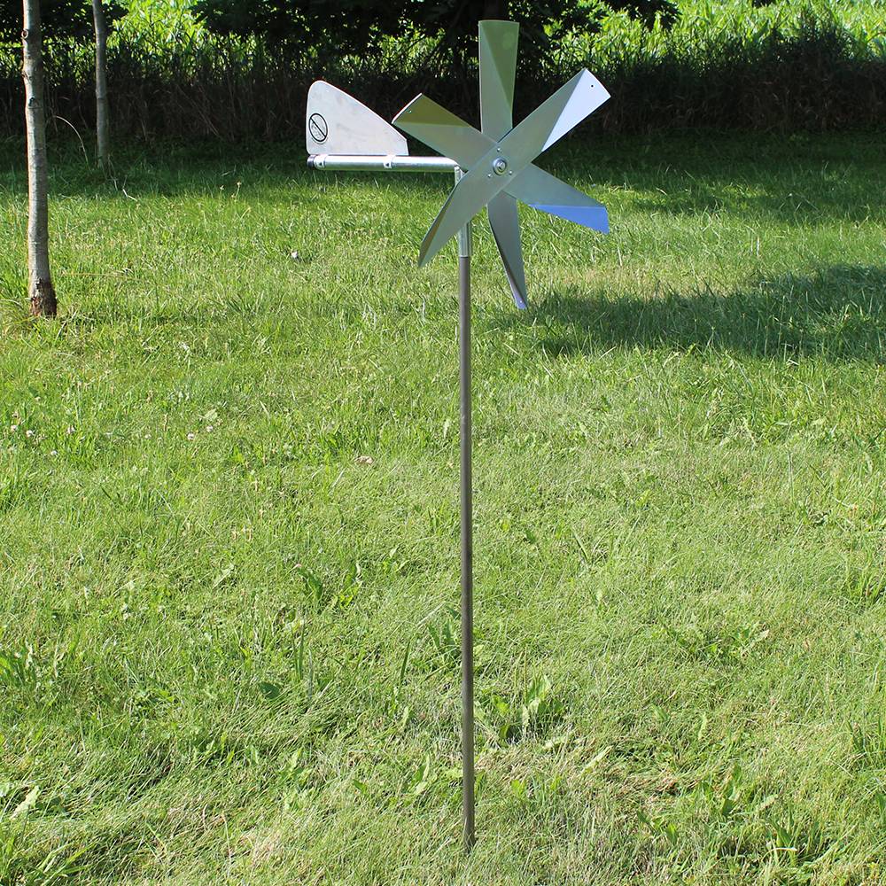 Metal windmill with spinning blades mounted on a slender pole standing in green lawn for pest control use