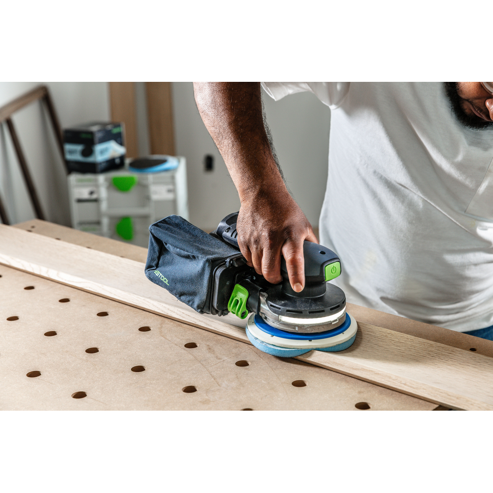 Person using Festool power sander with blue Granat PROfile abrasive disc on wooden plank in home improvement setting