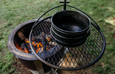 Black cast iron kettle hanging on grill rack above fire pit outdoors in backyard outdoor living setting