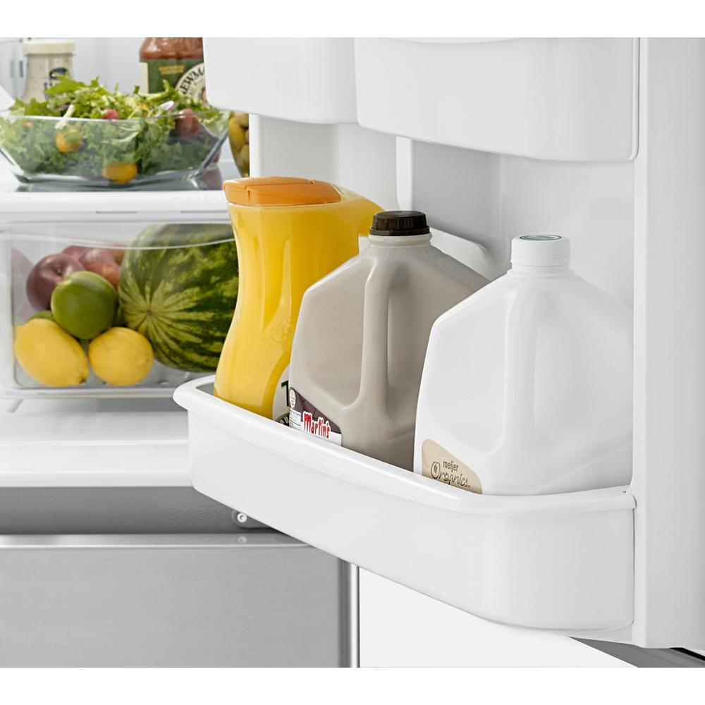 Close-up of refrigerator door shelf holding juice pitcher and milk gallons with fresh produce in background drawer