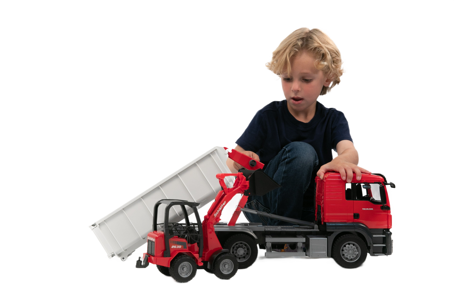 Child playing with red MAN truck and white roll-off container alongside compact loader for home improvement play