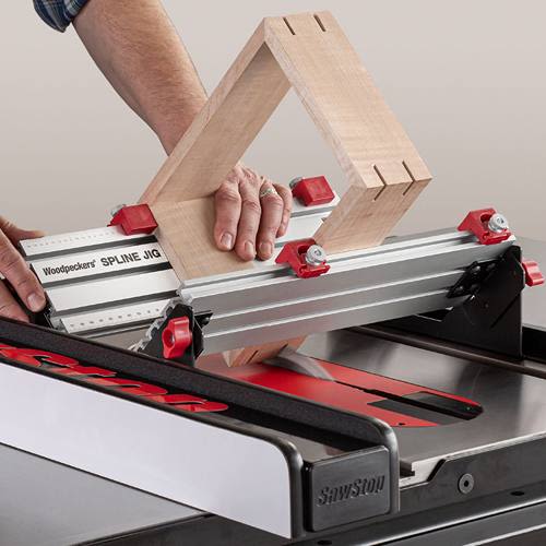 Aluminum spline jig with red adjustment knobs positioned on table saw for precise woodworking joinery tasks