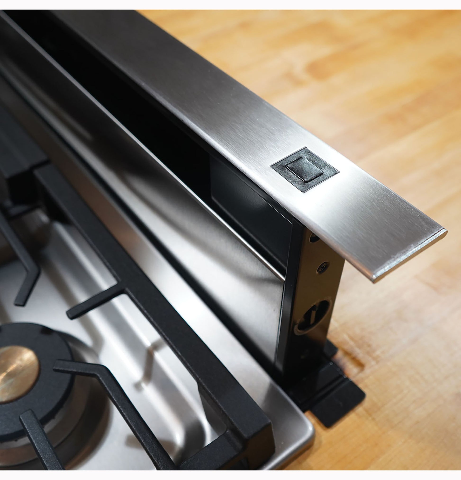 Stainless steel telescopic downdraft vent installed adjacent to a gas stove burner in kitchen appliance setting