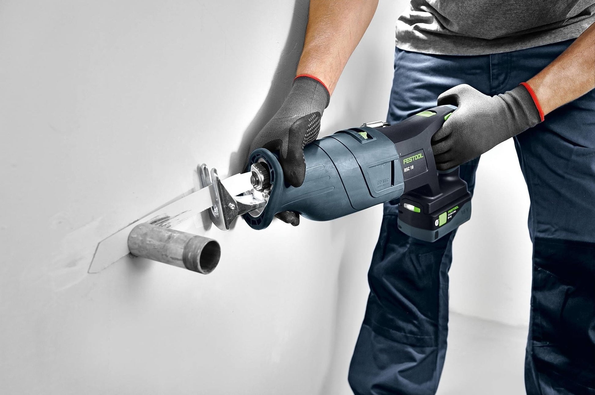Person using a Festool reciprocating saw with a metal cutting blade to cut through a metal pipe in a wall