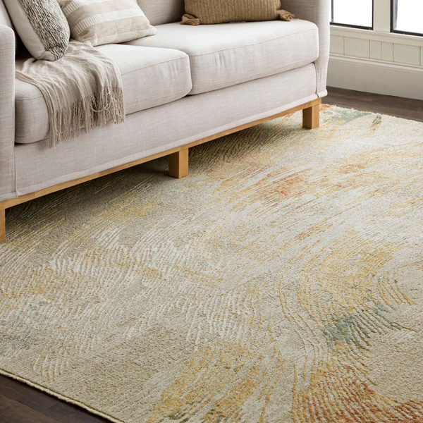 Beige area rug with subtle abstract pattern in muted earth tones placed beneath a light fabric sofa in a cozy living room