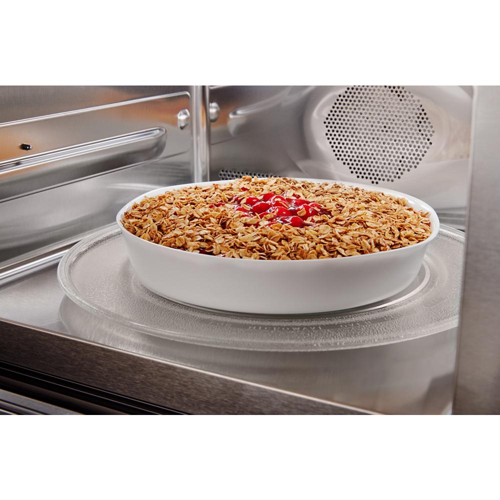 White ceramic dish with baked granola and cherries inside stainless steel microwave oven interior