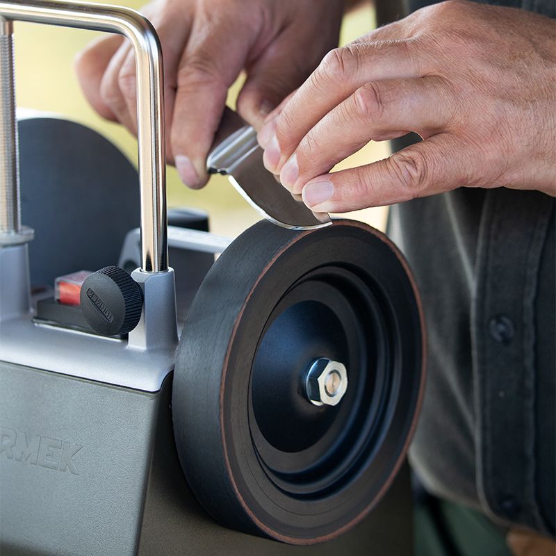 Hands sharpening a curved blade on a leather honing wheel attached to a Tormek sharpening tool for home improvement