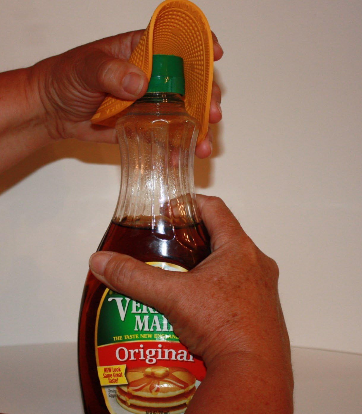 Hand using flexible textured grip pad to twist open a green-lidded bottle in kitchenware tools collection