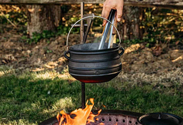 Black cast iron kettle with handle heating over outdoor fire pit in a backyard setting for outdoor living and fire pits