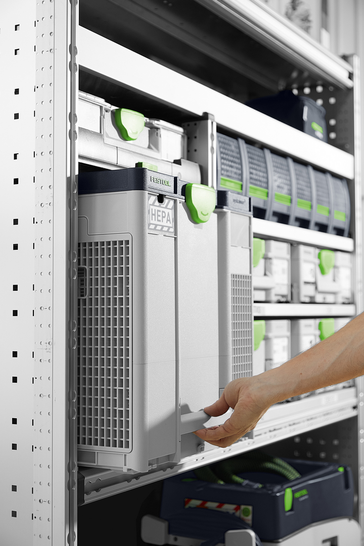 Person sliding a Festool air filtration unit with HEPA filter into a modular storage shelving system for tools and home improvement.