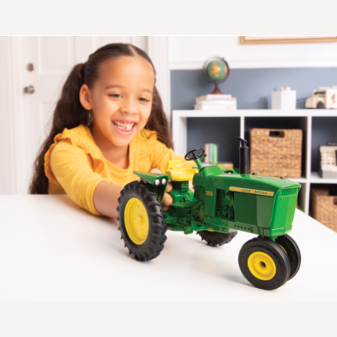 Child playing with a detailed green and yellow 1:16 scale model tractor on a white tabletop indoors