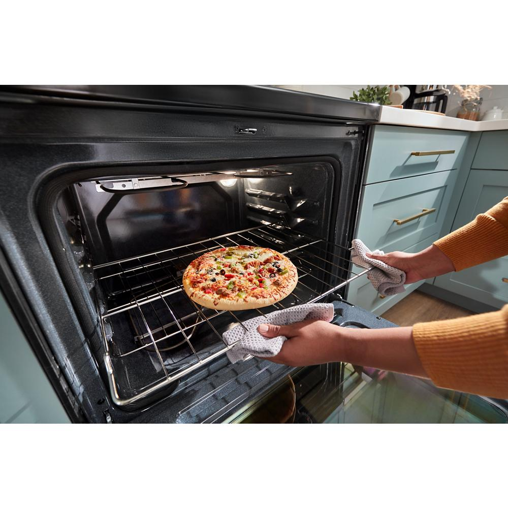 Person wearing gloves removing a pizza from a black electric oven in a modern kitchen with blue cabinets