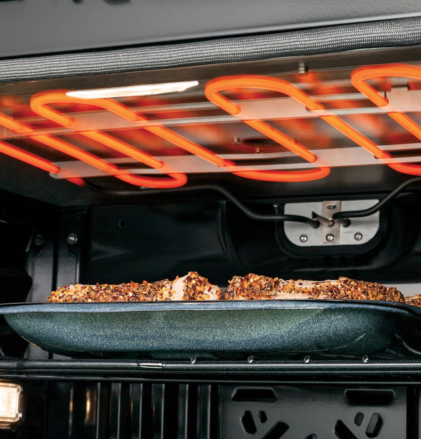 Close-up view of glowing convection heating element cooking seasoned food in built-in stainless steel oven interior
