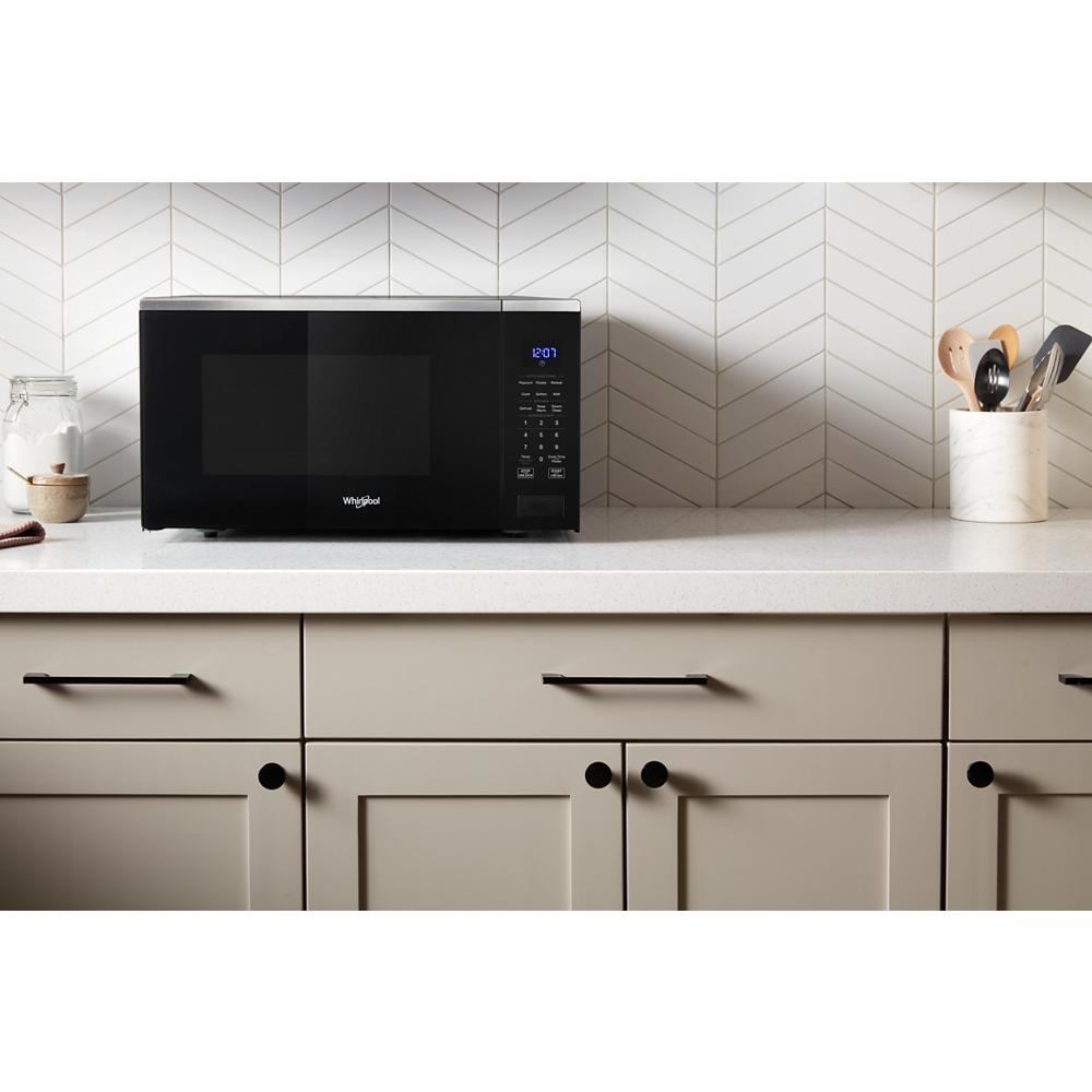 Black sensor cooking microwave with digital display and control panel on white kitchen countertop with beige cabinetry