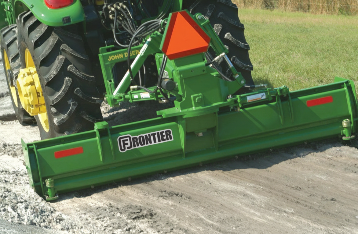 Green metal rear blade attachment with triangular safety reflector mounted on tractor for grading tasks