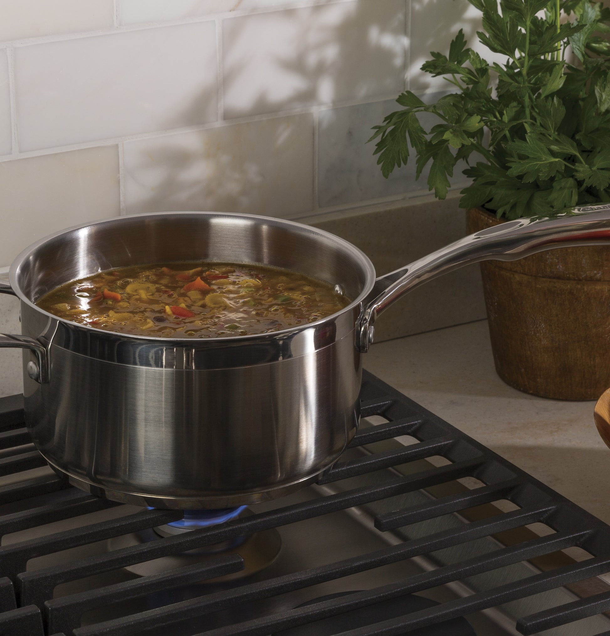 Stainless steel saucepan simmering vegetable soup on a gas burner of a built-in cooktop in kitchen setting
