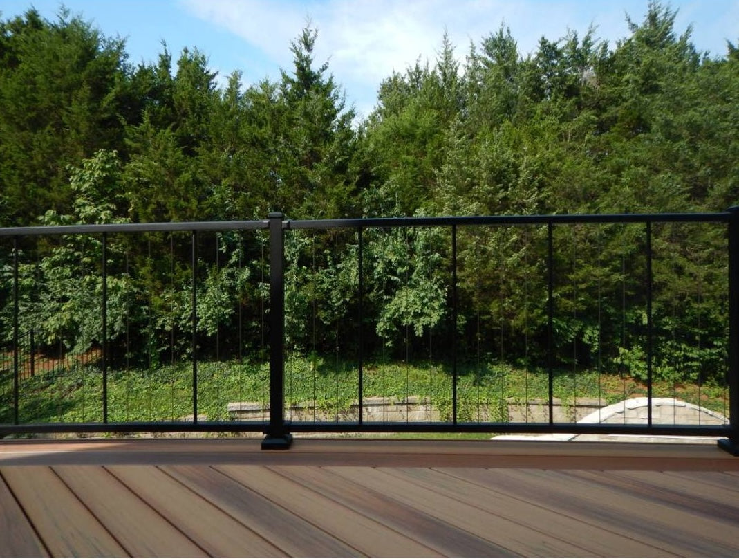 Black aluminum railing with vertical cables installed on wooden deck overlooking green wooded area for home improvement
