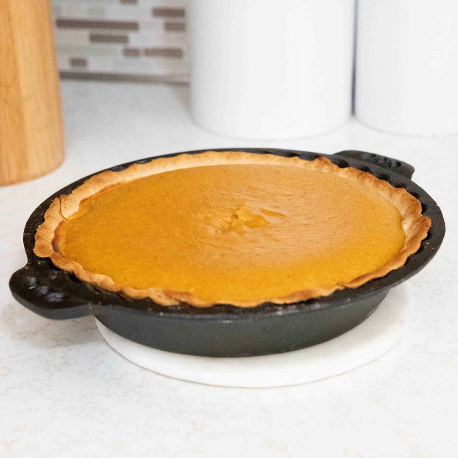 Rustic pumpkin pie baked in durable cast iron pan with crimped edges on white kitchen countertop under $50 collection