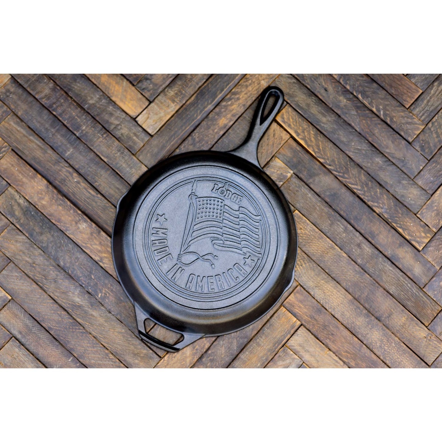 Seasoned cast iron skillet with embossed American flag and Made in America text on wooden herringbone surface kitchenware product