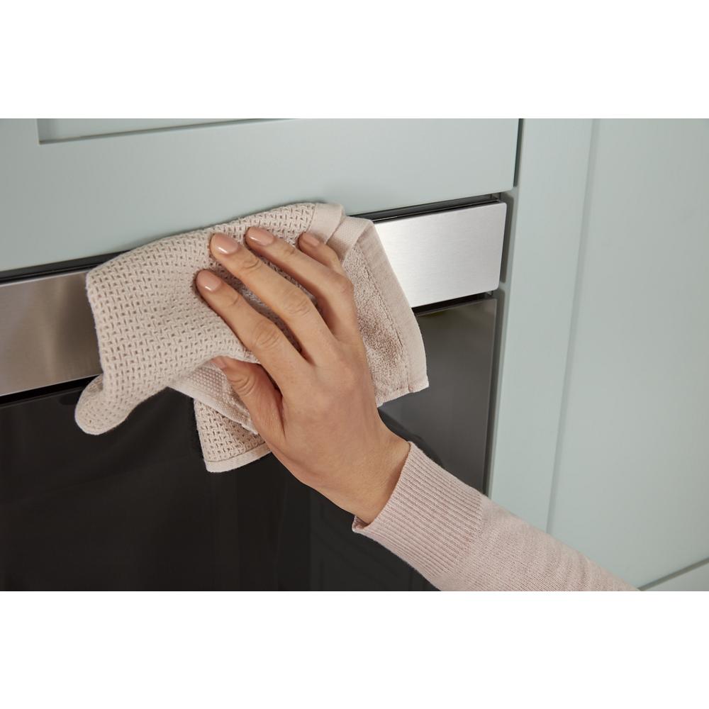 Hand cleaning stainless steel handle and black glass front of built-in microwave in modern kitchen setting