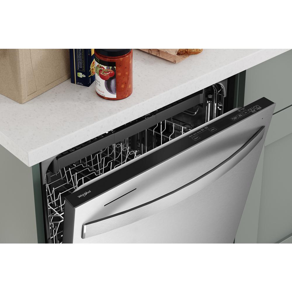Partially open stainless steel dishwasher integrated into green cabinetry with control panel on top edge in kitchen setting