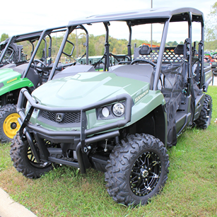 Green John Deere off-road utility vehicle with four seats and heavy-duty tires parked on grass outdoors