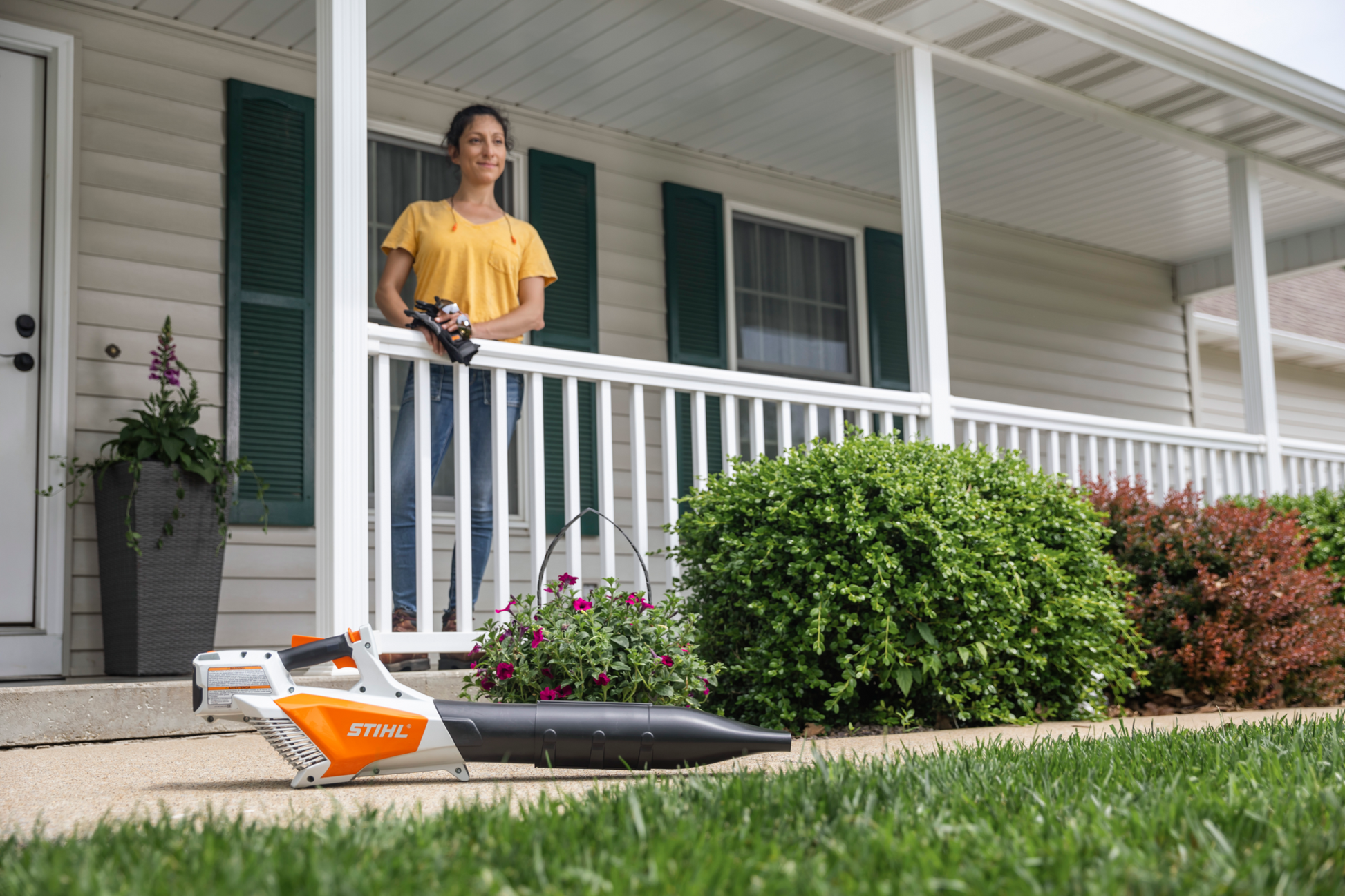 Woman using a cordless orange and white handheld blower to clear debris in a residential yard for home improvement tasks