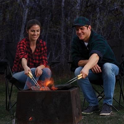 Two people cooking sandwiches outdoors over a campfire using a cast iron double sandwich cooker with long handles