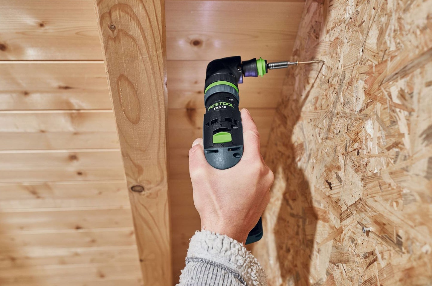 Compact cordless drill with angled design driving a screw into plywood in woodworking and power tools setting