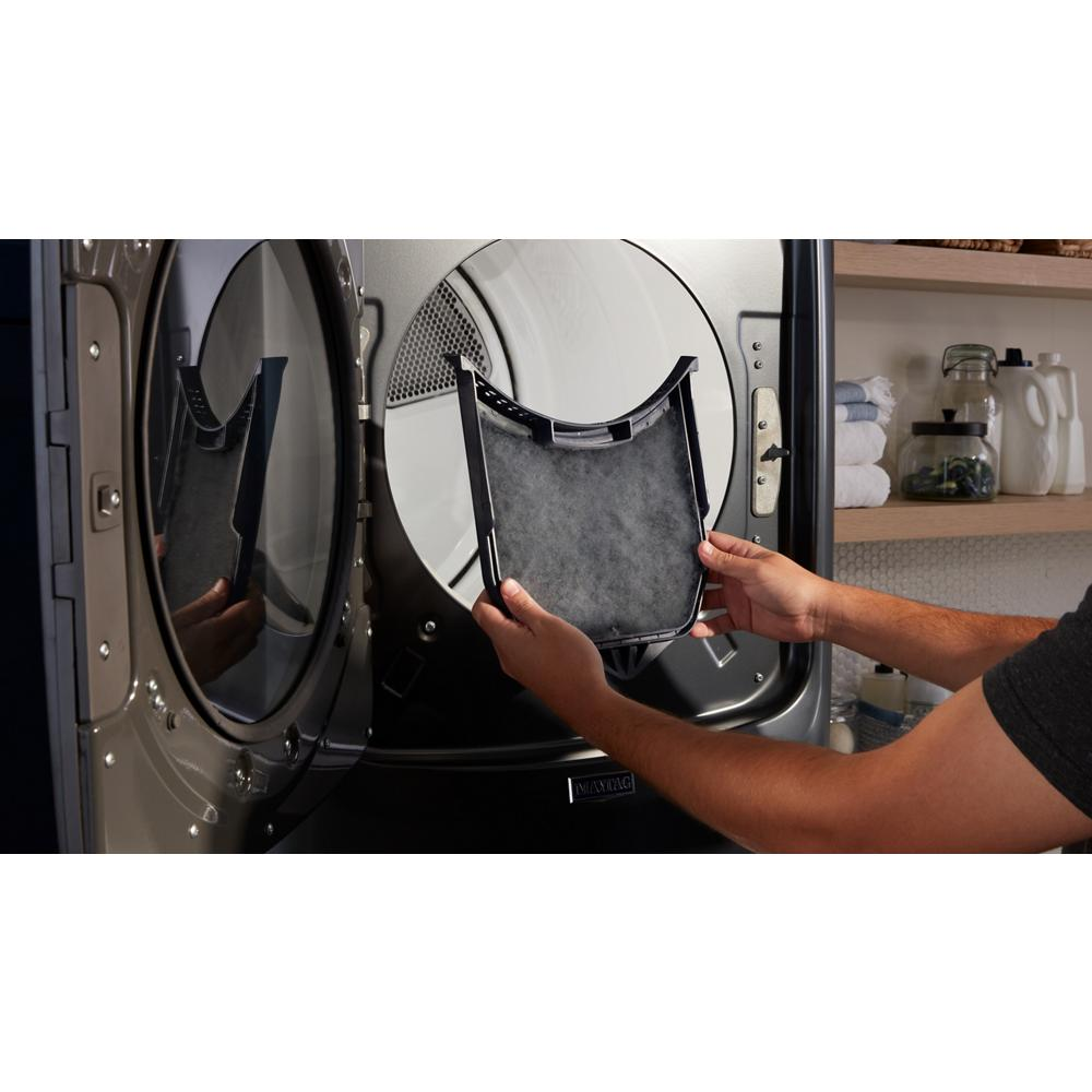 Hand removing a reusable lint filter from a front load washer in a modern laundry room with shelves and supplies visible