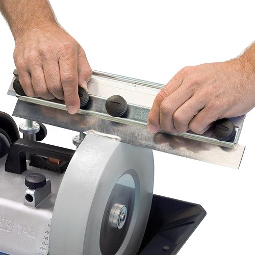 Hands adjusting metal planer blade jig on grinding wheel for precise sharpening in home tool workshop