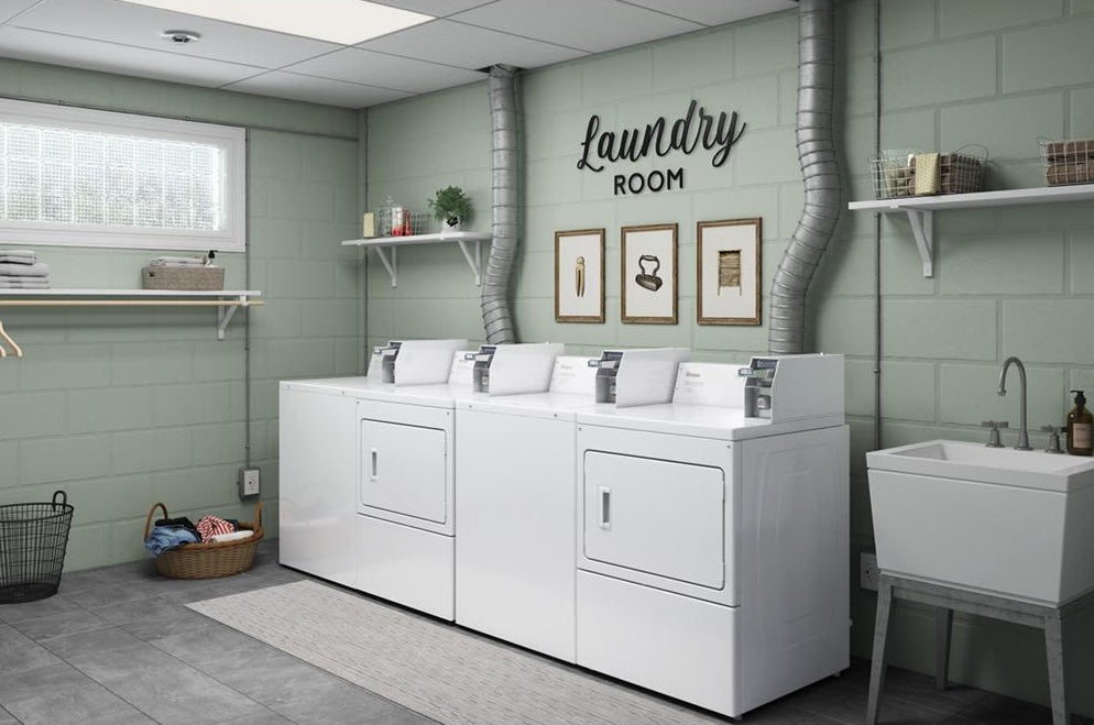 Row of white commercial top-load washers with coin slide controls in a clean laundry room setting
