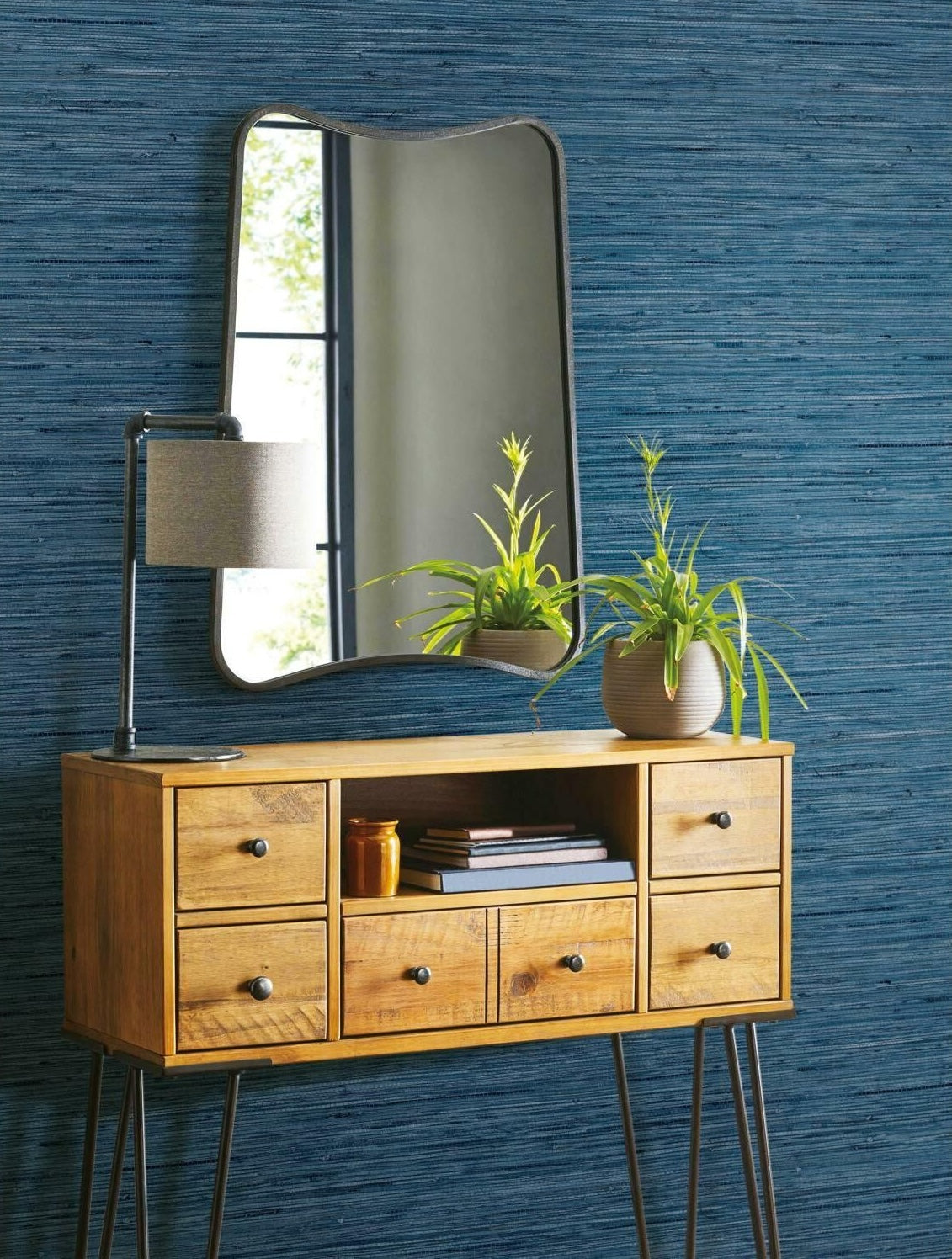 Blue grasscloth textured peel and stick wallpaper behind wooden console table with mirror and potted plant decor