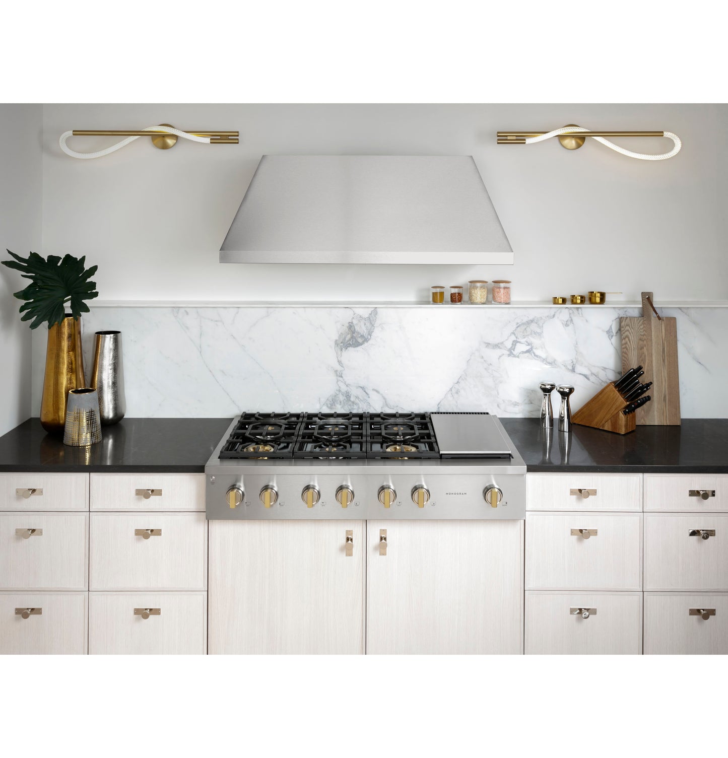 Modern stainless steel gas rangetop with six burners, griddle, and brushed gold control knobs in kitchen setting