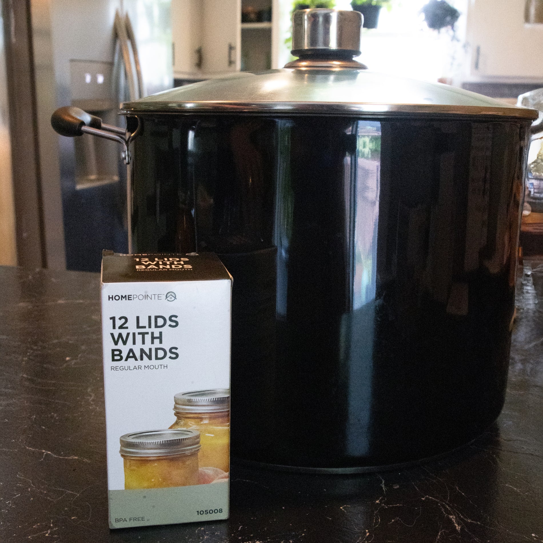 Box of 12 regular-mouth canning jar lids and bands displayed in front of a large black water bath canner, ideal for Kitchenware and Under $50 collections.