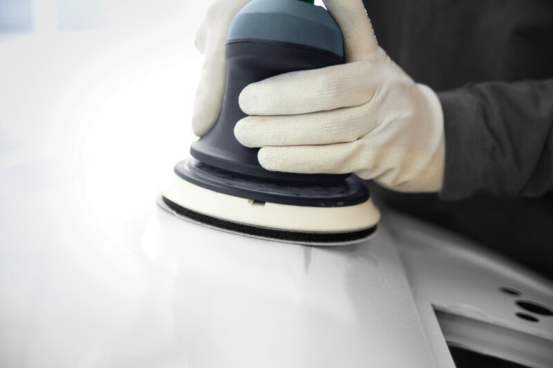 Handheld electric sander with white backing pad smoothing a painted surface for tools and home improvement use