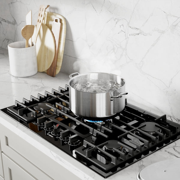 Black gas cooktop with five burners and stainless steel pot boiling water on marble countertop surface