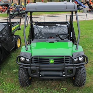 Green work utility vehicle with protective canopy and rugged tires parked on grass near outdoor equipment display