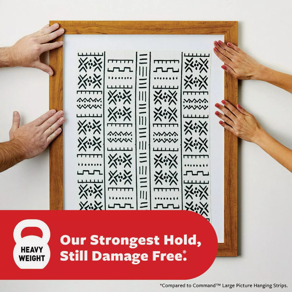 Hands placing a wood-framed black and white patterned print on a white wall using damage-free hanging strips from hardware collections