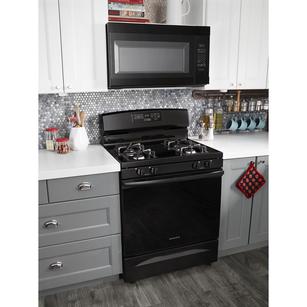 Black freestanding gas range with four burners and digital control panel installed between gray cabinets and white countertops