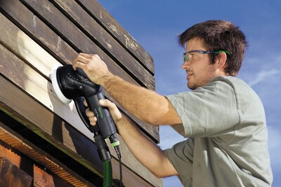 Man using a Festool multi-mode sander on wooden exterior siding for tools and home improvement tasks