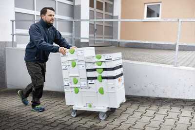 Man pushing a wheeled cart stacked with modular tool storage boxes for workshop organization and tool storage solutions
