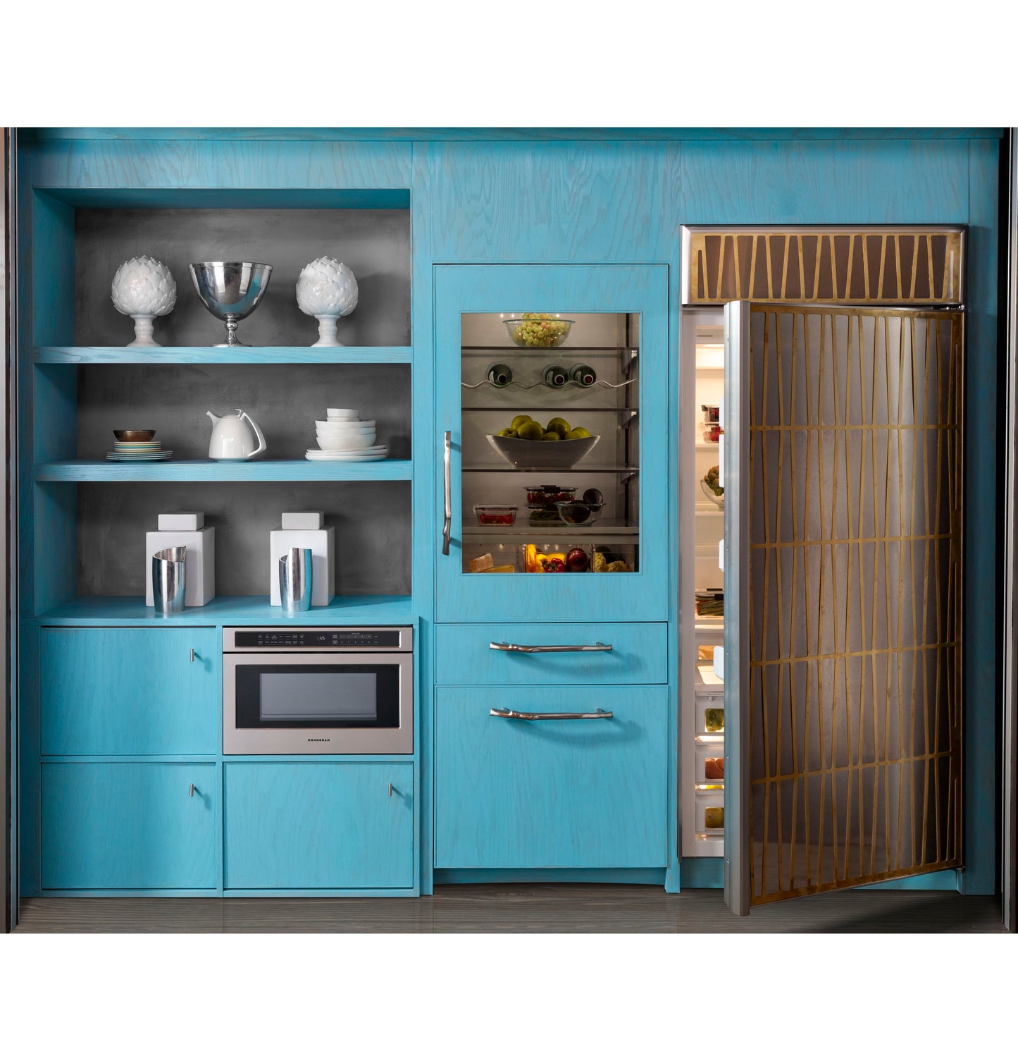 Built-in microwave drawer integrated into modern blue kitchen cabinetry beside a patterned gold refrigerator door open to show contents