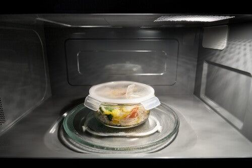 Interior view of a microwave with sensor cooking heating a covered bowl of mixed vegetables inside the appliance