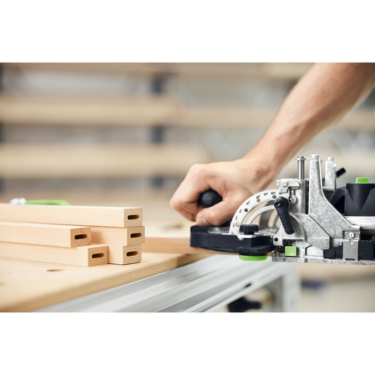 Close-up of a person using a Festool DOMINO joiner to create precise mortise joints on wooden boards in a well-lit woodworking workshop, part of power and woodworking tools collections.