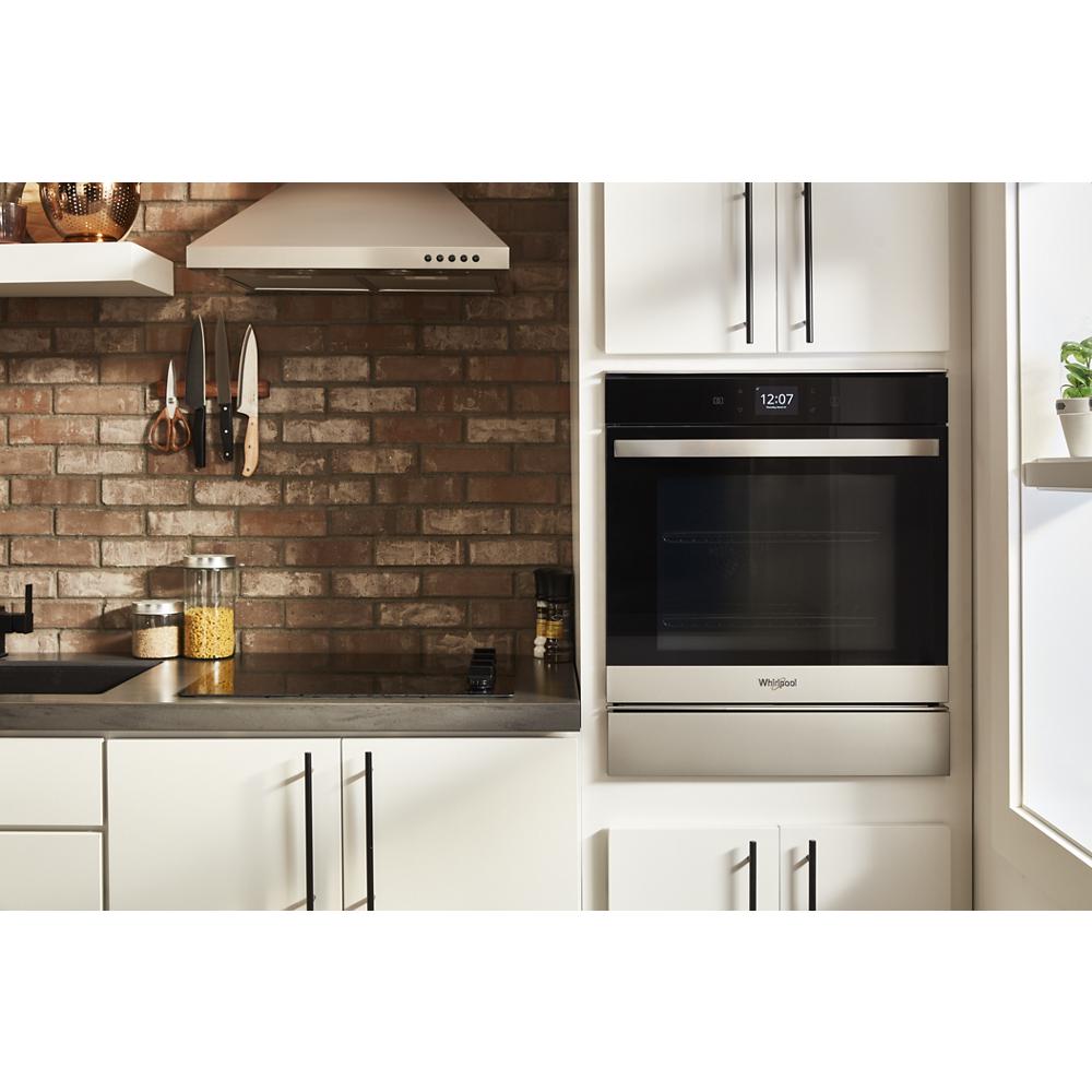 Built-in stainless steel convection oven installed in a white kitchen with brick backsplash and black countertop
