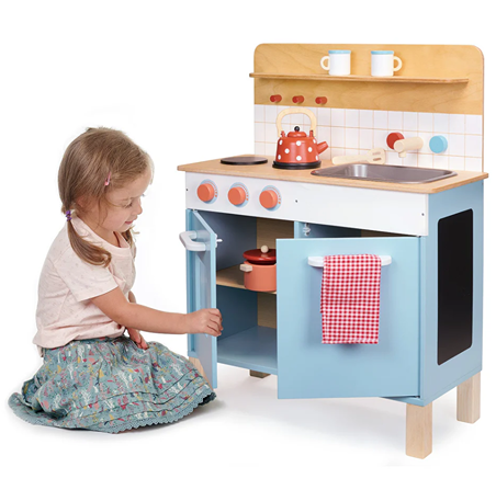 Child playing with wooden play kitchen in pastel colors featuring pots, kettle, and shelves for pretend play toys in Toys & Games